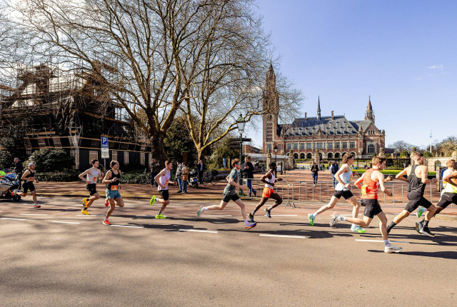 Atleten rennen tijdens een wedstrijd in Den Haag, met het Vredespaleis op de achtergrond.