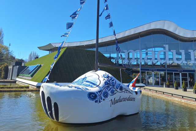 Een grote houten schoenboot voor Madurodam met vlaggen en het gebouw op de achtergrond.