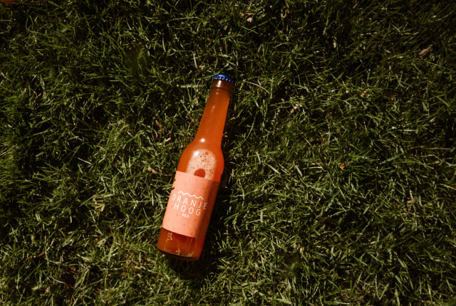 Een fles Oranje Hoog pils ligt op het gras.