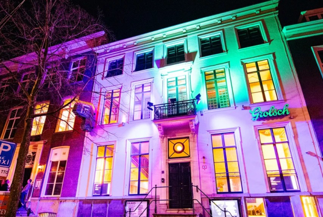 Een kleurrijk verlichte gevel van een gebouw met het woord 'Grolsch' zichtbaar.