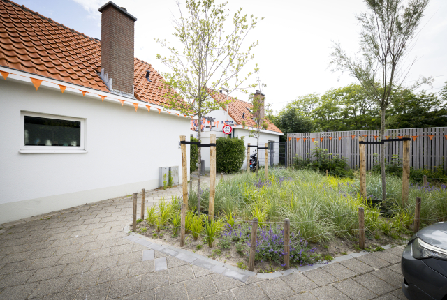 Een huis op Scheveningen met een rood dak en een groene tuin met bloemen.