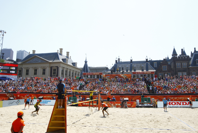 Spelers in oranje shirts tijdens beachvolleybalwedstrijd.