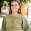 Vrouw met lange, golvende haren en een groene blouse, lachend op straat.