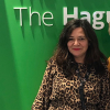 Vrouw in een dierenprint jurk poseert voor een groene muur met teksten over Den Haag.