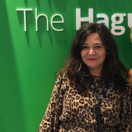 Vrouw in een dierenprint jurk poseert voor een groene muur met teksten over Den Haag.