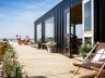 Mensen lekker genietend van de zon op het zij-terras van The Shore op Scheveningen. Deze duurzame strandtent bevindt zich in een container.
