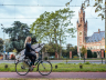 Zomer in Den Haag. Meisje met surfplank onder haar arm fiets langs het Vredespaleis richting Scheveningen