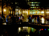 Wandelaars met lichtjes steken ’s avonds een brug over in een verlichte stad