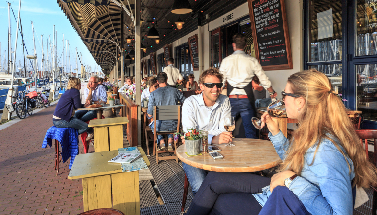 Zicht op restaurants en en mensen die een drankje drinken op terrassen langs de haven van Scheveningen op een zonnige dag
