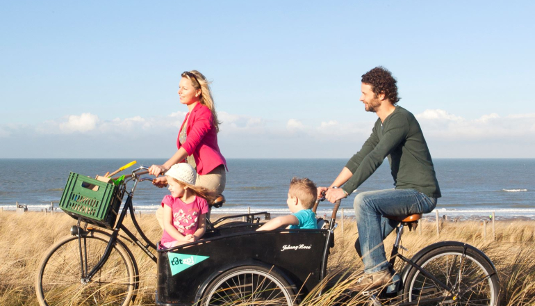 Fietsend stel met kinderen in de bakfiets in de duinen 