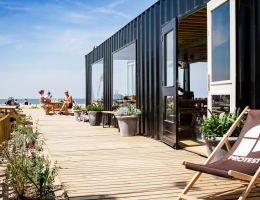 Mensen lekker genietend van de zon op het zij-terras van The Shore op Scheveningen. Deze duurzame strandtent bevindt zich in een container.