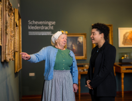 Vrouw in klederdracht wijst iets aan op een schilderij in Muzee Scheveningen