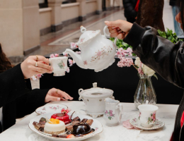 Twee mensen genieten van een high tea aan een sfeervol gedekte tafel in De Passage, met porseleinen servies, luxe taartjes en chocolade, terwijl thee wordt ingeschonken. Twee mensen genieten van een high tea aan een sfeervol gedekte tafel in De Passage, met porseleinen servies, luxe taartjes en chocolade, terwijl thee wordt ingeschonken.