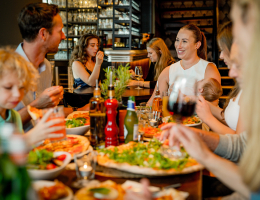 Gezellige familiescène in een restaurant waar mensen genieten van verse pizza en elkaars gezelschap. Een warme, ontspannen sfeer met lachende gezichten.