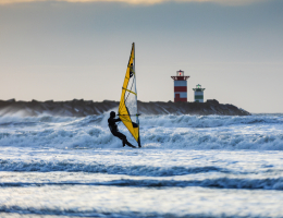 Surfer in zee bij Scheveningen bij het Noordelijk Havenhoofd met het rode havenlicht op de achtergrond. 