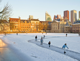 Mensen aan het schaatsen op de bevroren Hofvijver in Den Haag met de moderne skyline op de achtergrond