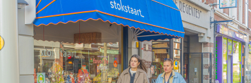 Twee mensen lopen over straat, achter hen een blauwe markies