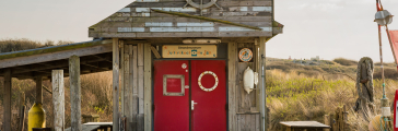 Wooden beach house with a red door and a steering wheel on top.