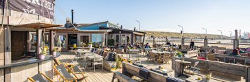 Zonnige terras van Hart Beach met ligstoelen en houten tafels