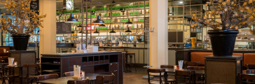 Industriele interieur van grand café Dudok met zich op de bar en lege houten stoelen en tafeltjes.