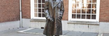 Brons standbeeld van een man in een lange jas en hoed